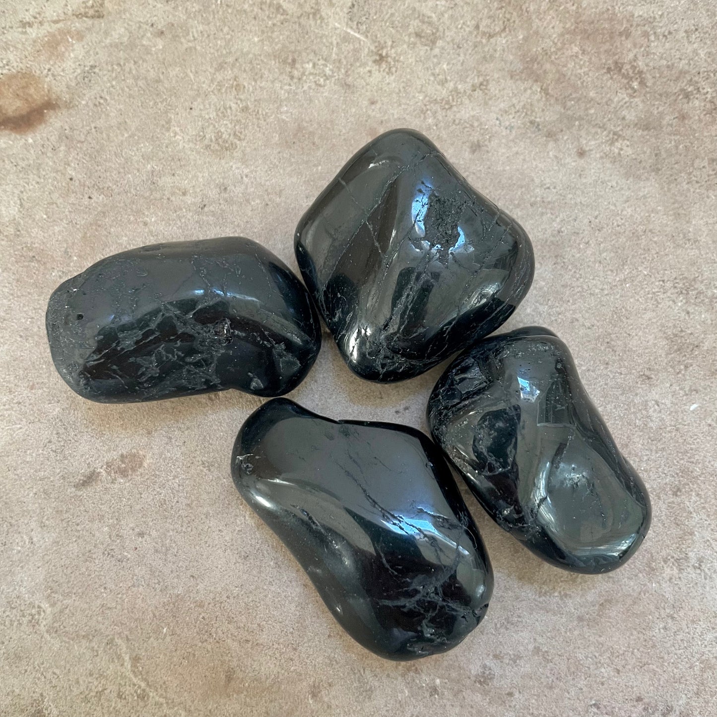 Black Tourmaline Tumbles on a stone background.