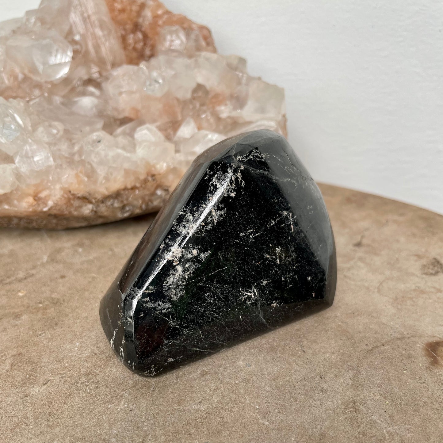 Black Tourmaline Free Form on a stone bench in front of a crystal cluster.