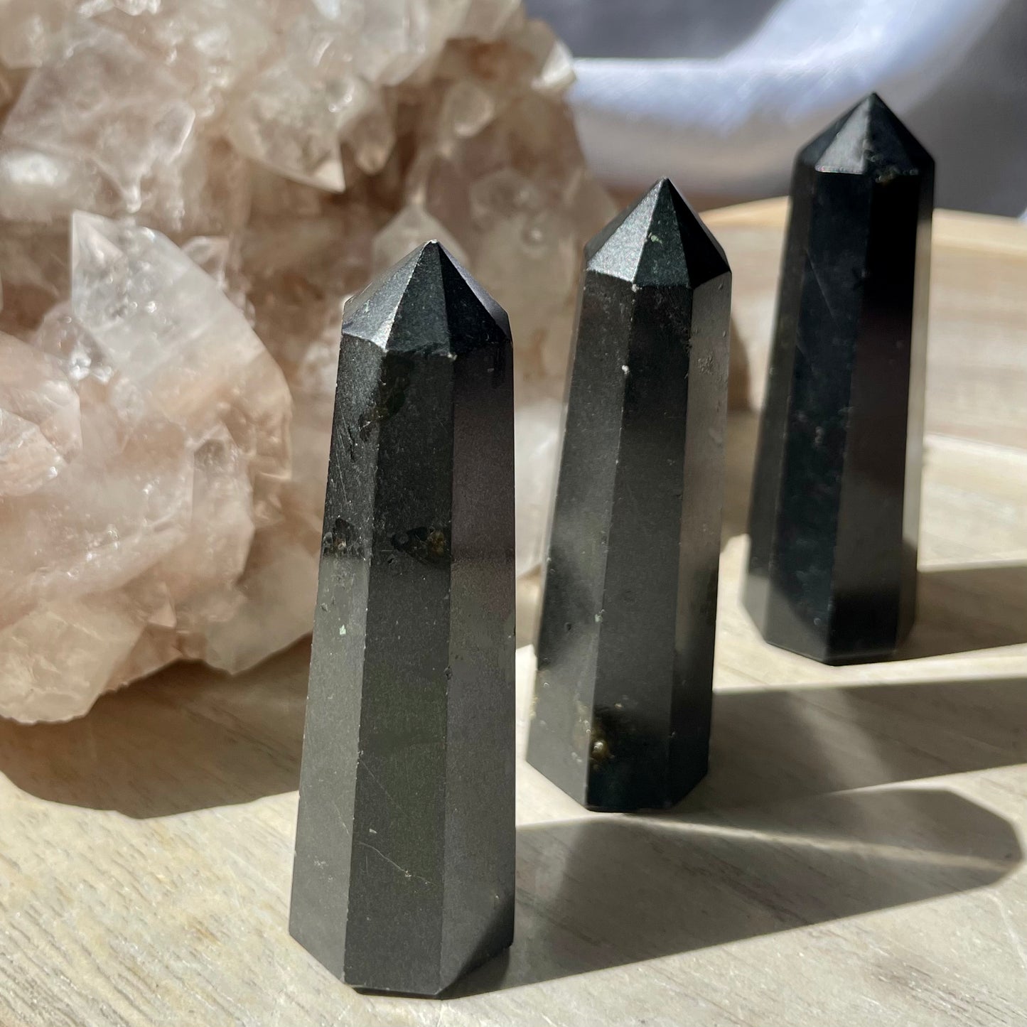 Three Black Tourmaline Towers sitting on a wooden bench in front of a crystal cluster.