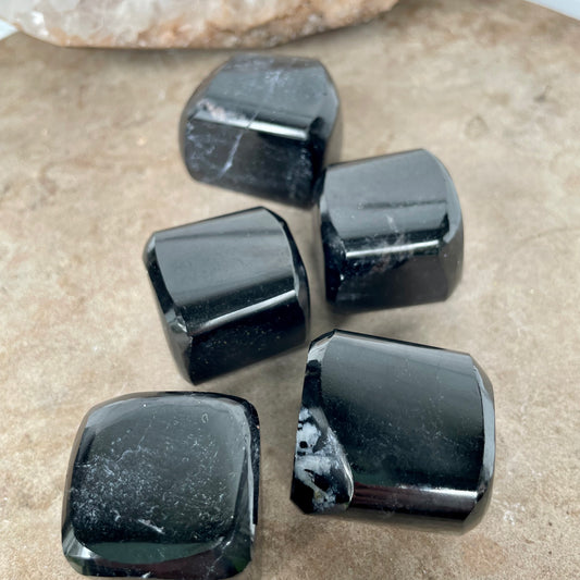 Five Black Tourmaline Free Form Cubes sitting on a stone bench. 
