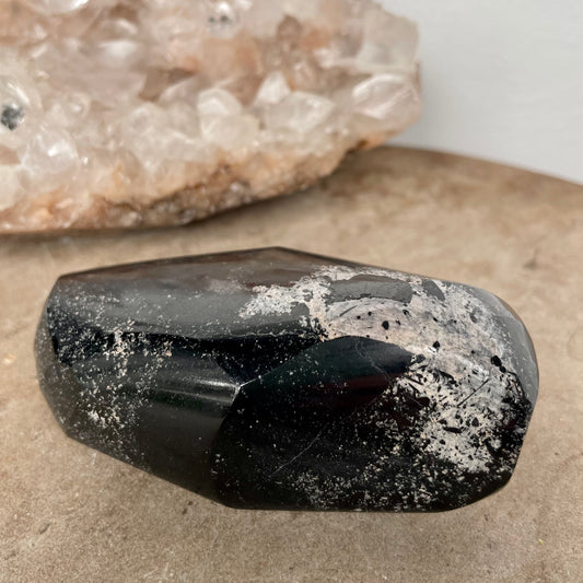 Black Tourmaline Free Form on a stone bench in front of a crystal cluster.