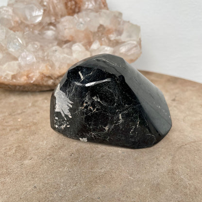 Black Tourmaline Free Form on a stone bench in front of a crystal cluster.