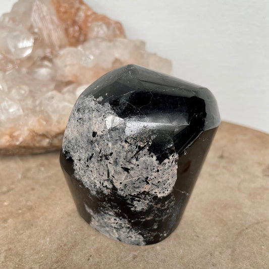 Black Tourmaline Free Form on a stone bench in front of a crystal cluster.