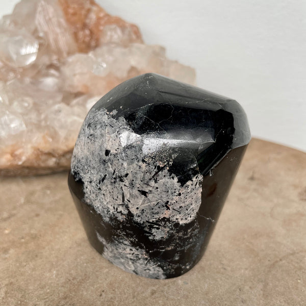 Black Tourmaline Free Form on a stone bench in front of a crystal cluster.