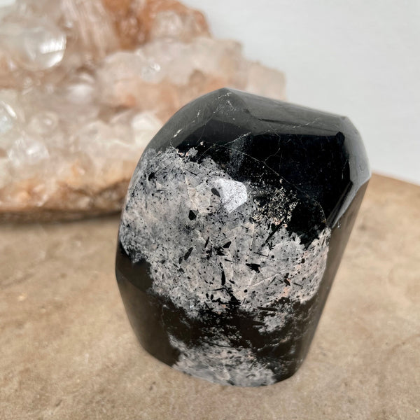 Black Tourmaline Free Form on a stone bench in front of a crystal cluster.
