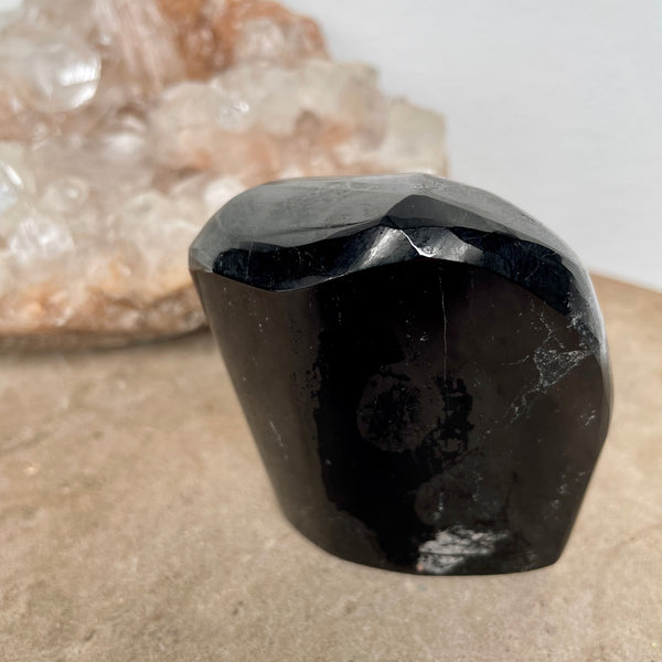 Black Tourmaline Free Form on a stone bench in front of a crystal cluster.