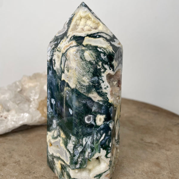 Moss Agate Tower standing on stone bench in front of crystal cluster