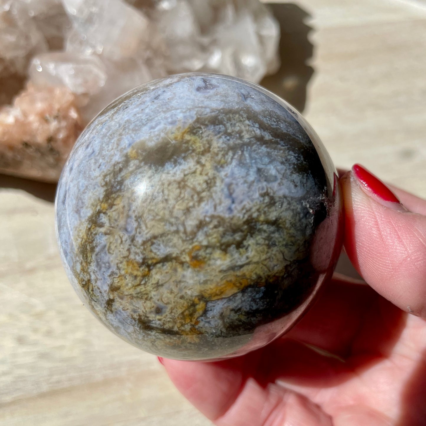 Hand holding Moss Agate Purple Sphere on wooden background