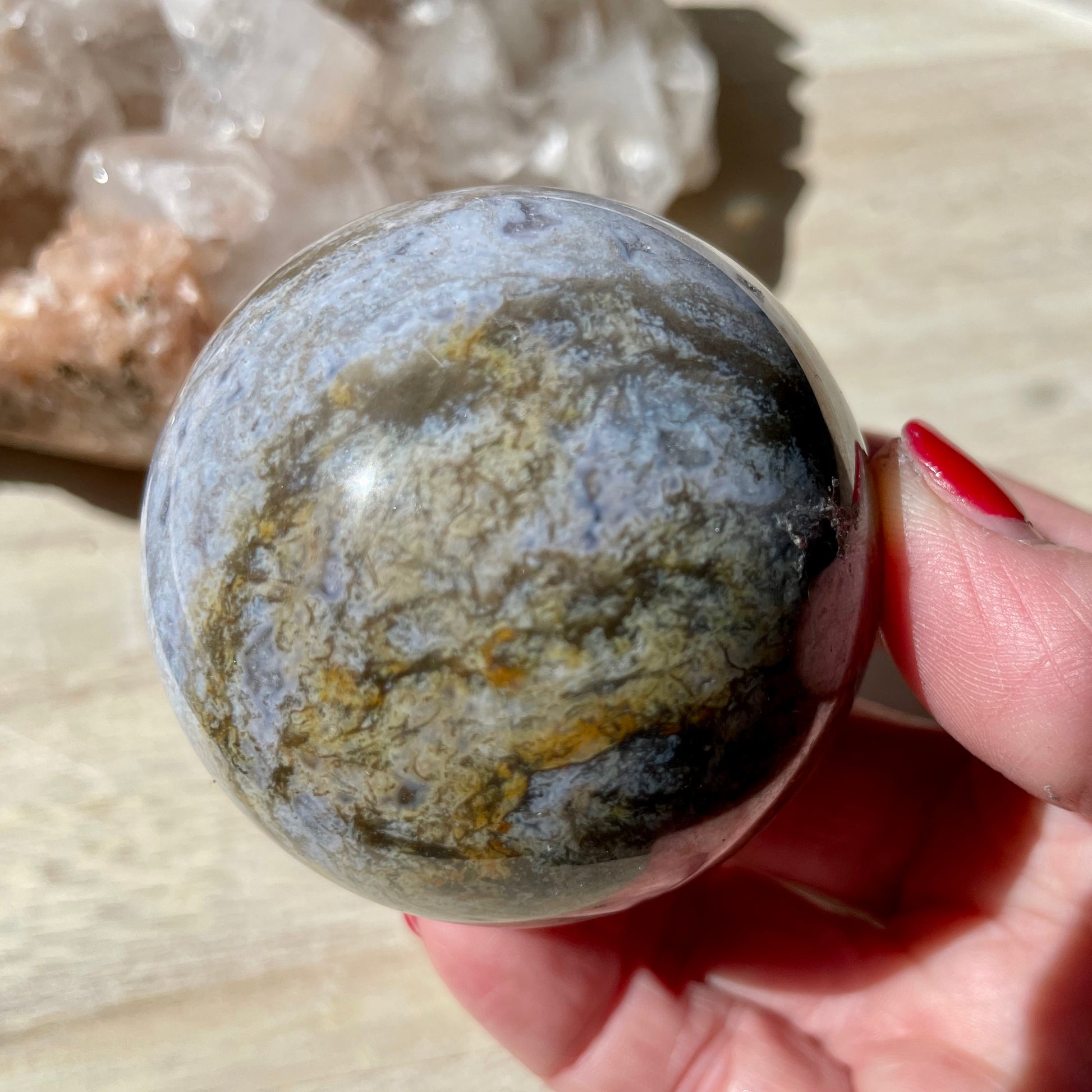 Hand holding Moss Agate Purple Sphere on wooden background