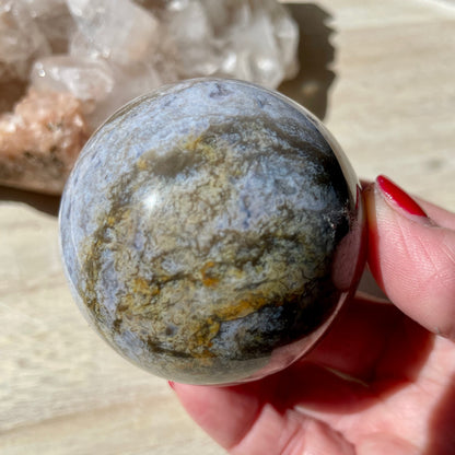 Hand holding Moss Agate Purple Sphere on wooden background