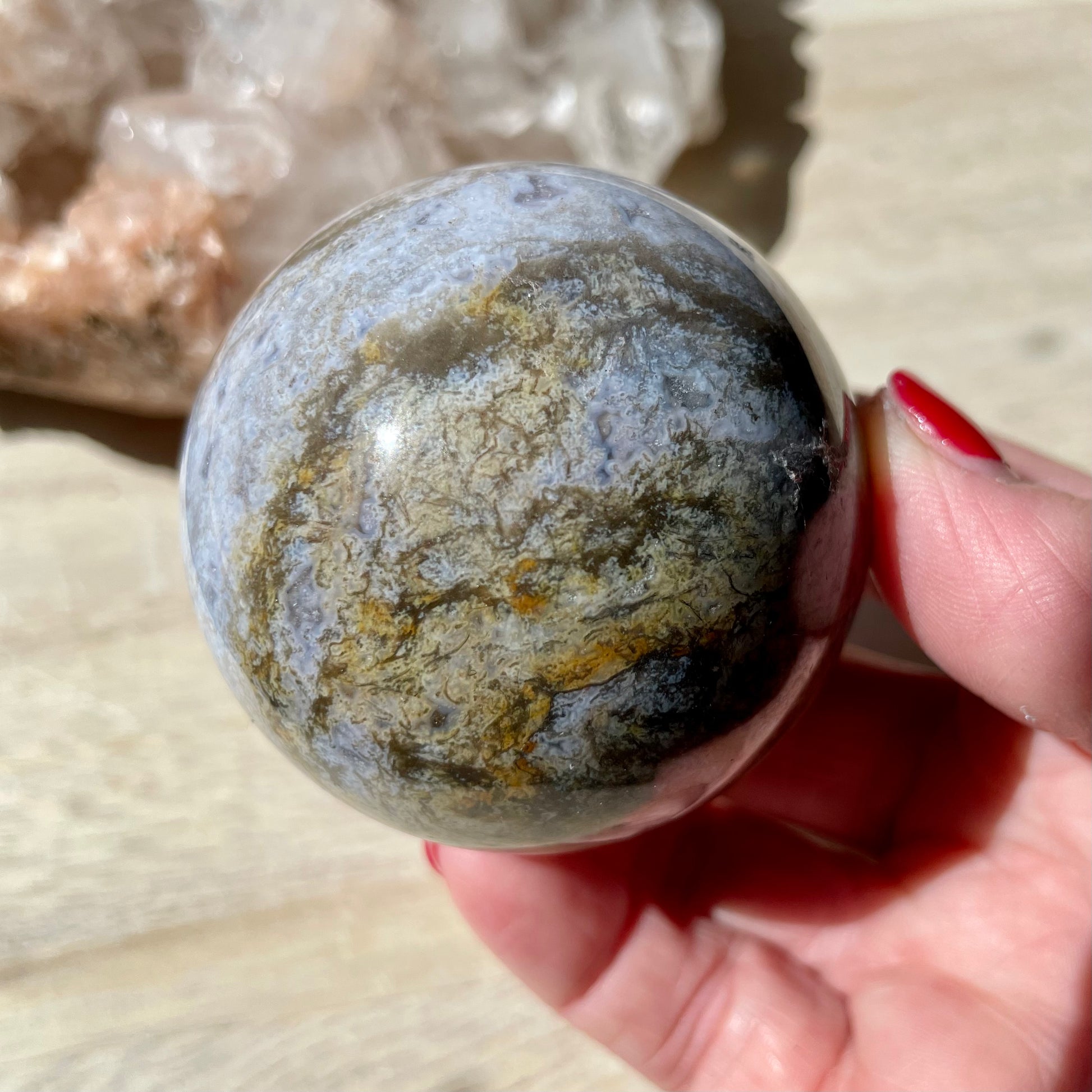 Hand holding Moss Agate Purple Sphere on wooden background