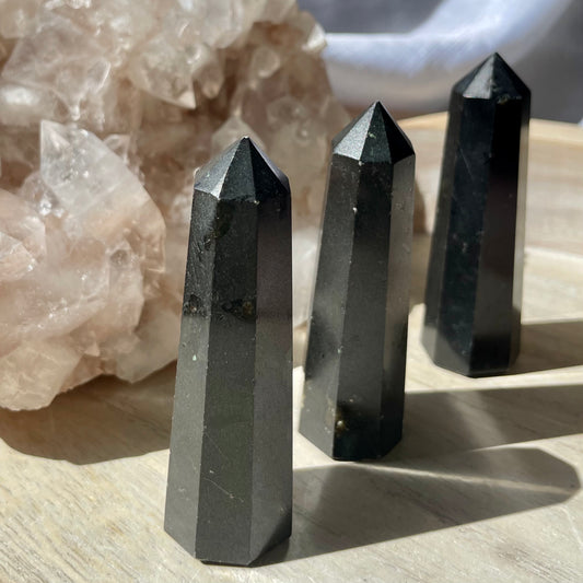 Three Black Tourmaline Towers sitting on a wooden bench in front of a crystal cluster.