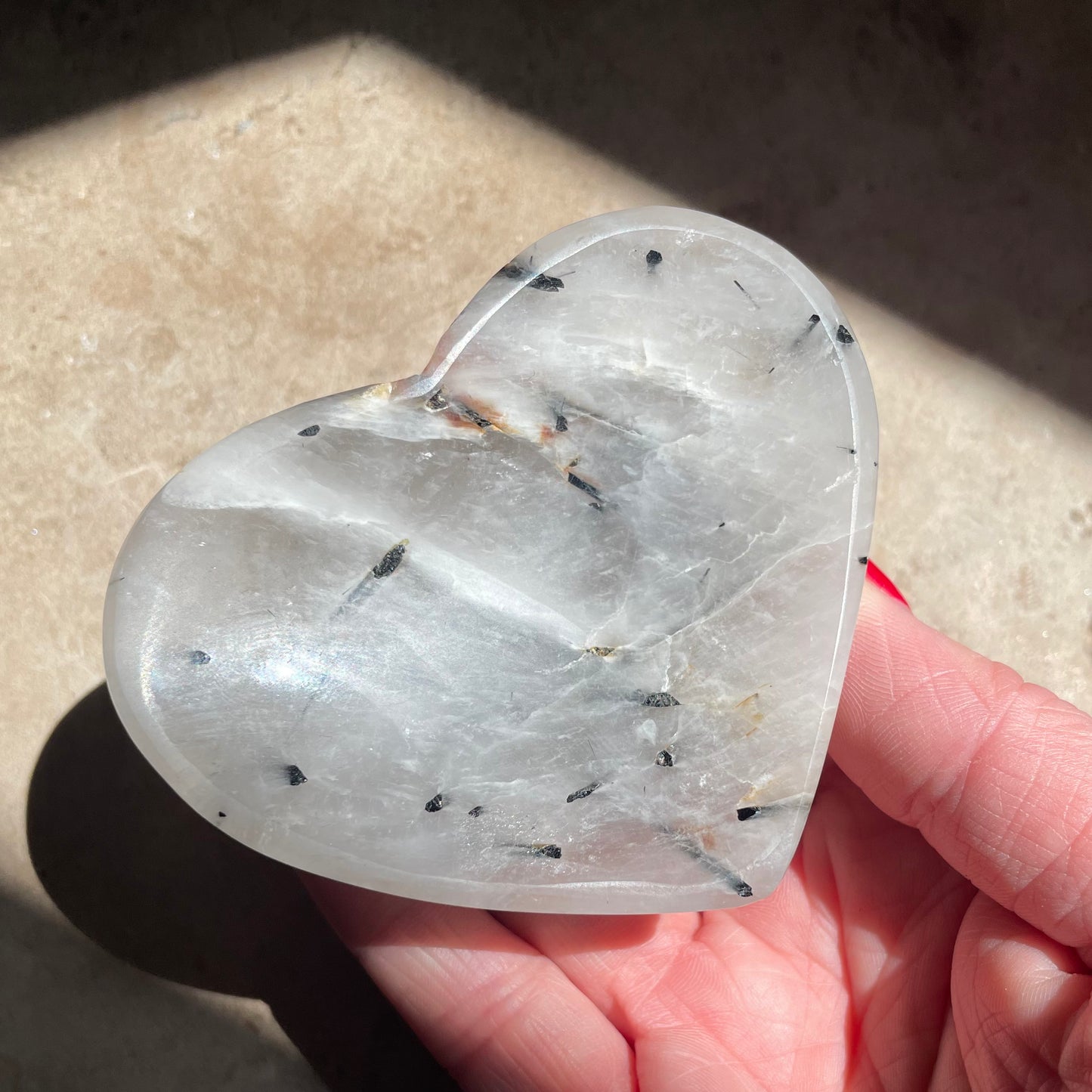 A hand holding Tourmaline Quartz Heart Bowl 8cm on stone background