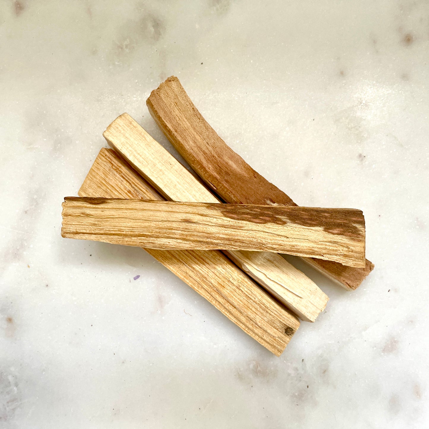 Four Palo Santo sticks on a stone bench.