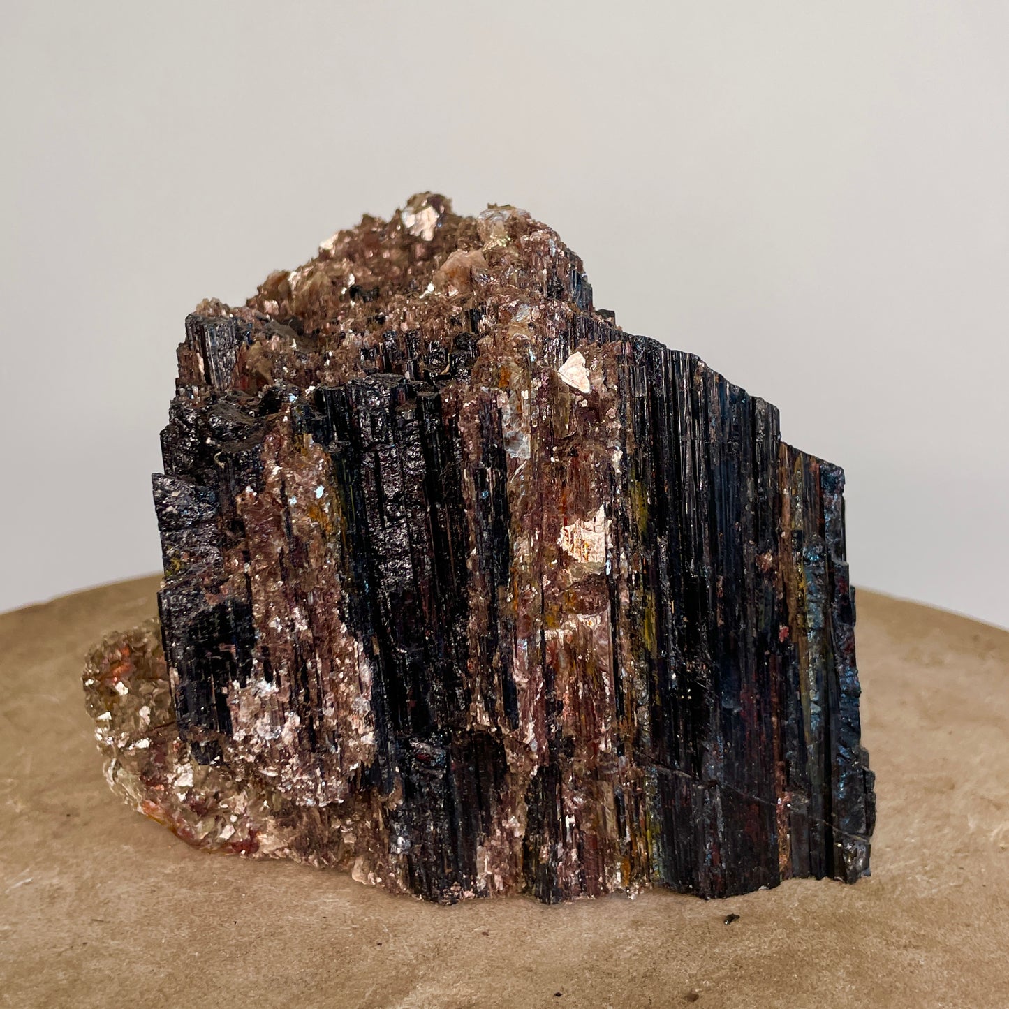 Black Tourmaline and Mica Cluster sitting on a stone with a white background.