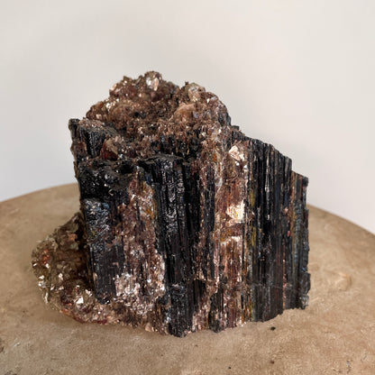 Black Tourmaline and Mica Cluster sitting on a stone with a white background.