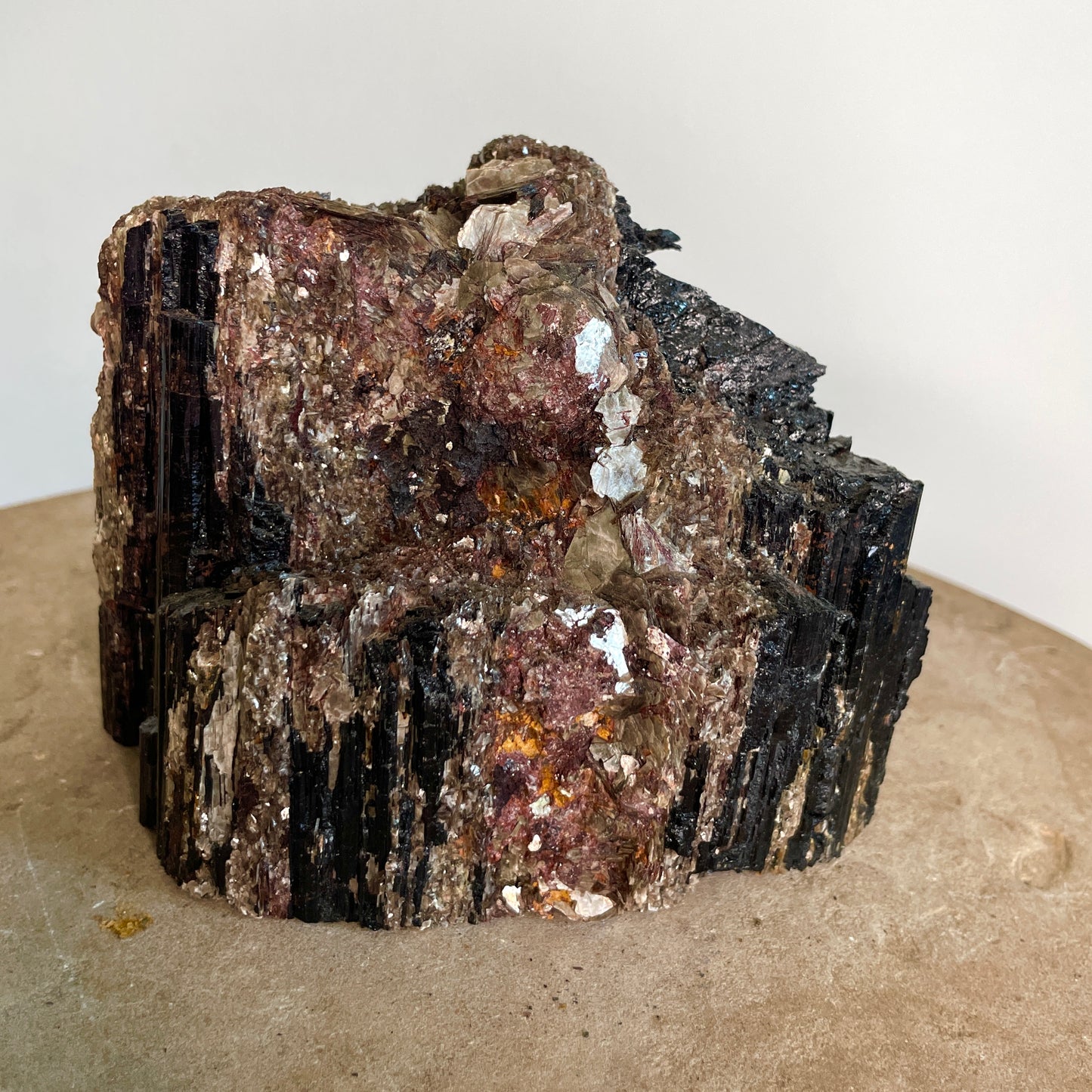 Black Tourmaline and Mica Cluster sitting on a stone with a white background.