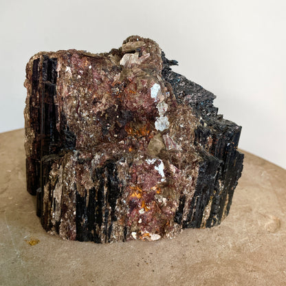 Black Tourmaline and Mica Cluster sitting on a stone with a white background.