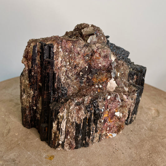 Black Tourmaline and Mica Cluster sitting on a stone with a white background.