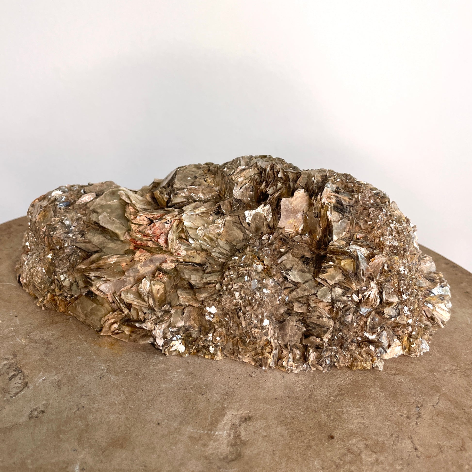Black Tourmaline and Mica Cluster sitting on a stone with a white background.