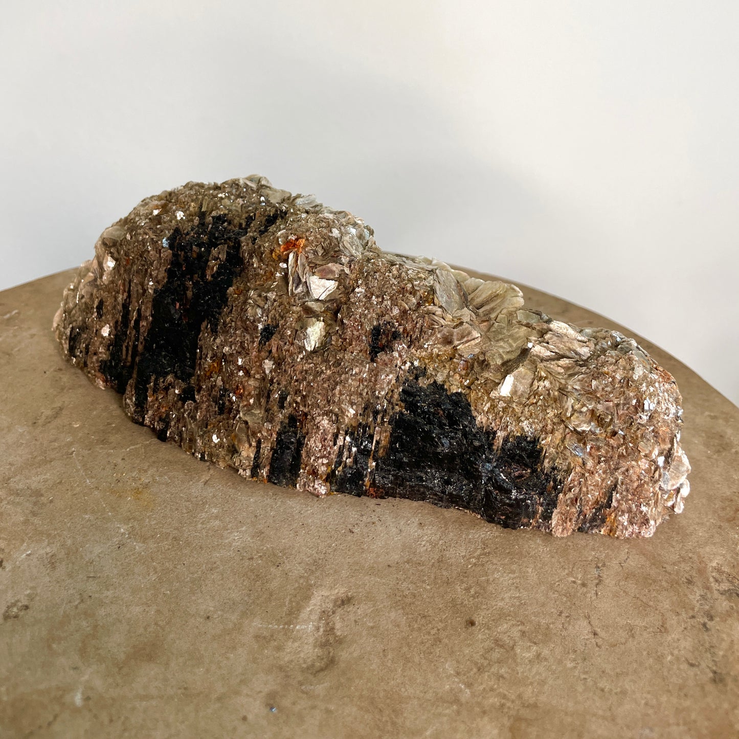 Black Tourmaline and Mica Cluster sitting on a stone with a white background.