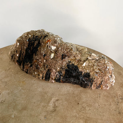Black Tourmaline and Mica Cluster sitting on a stone with a white background.