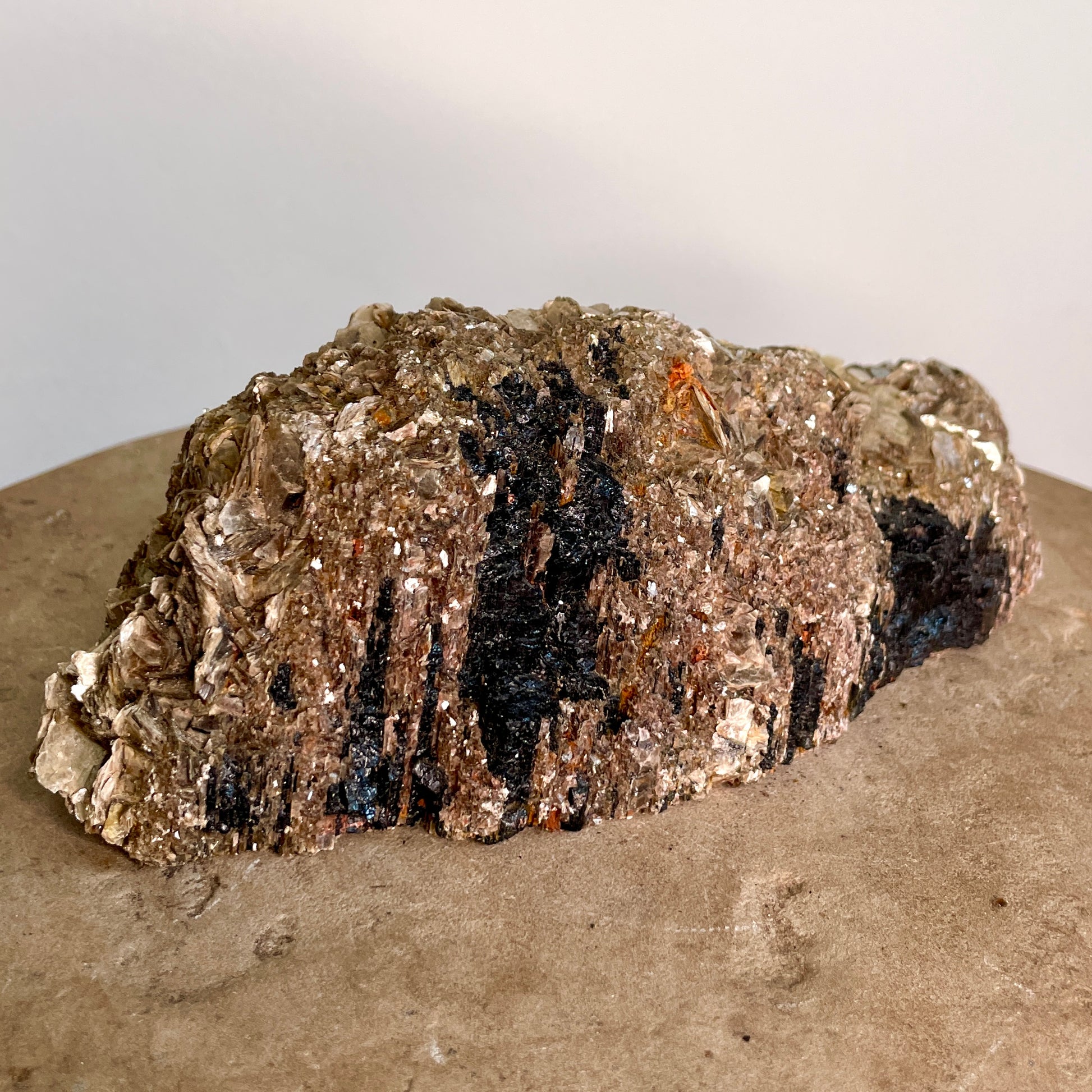 Black Tourmaline and Mica Cluster sitting on a stone with a white background.