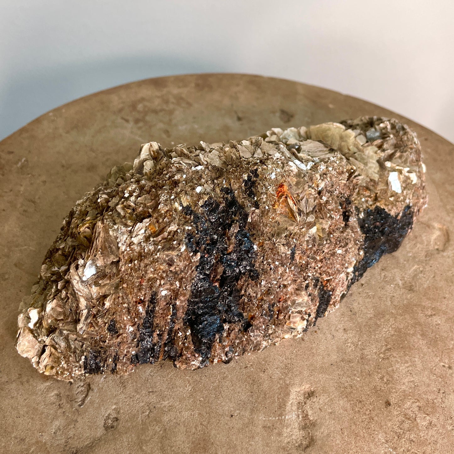 Black Tourmaline and Mica Cluster sitting on a stone with a white background.