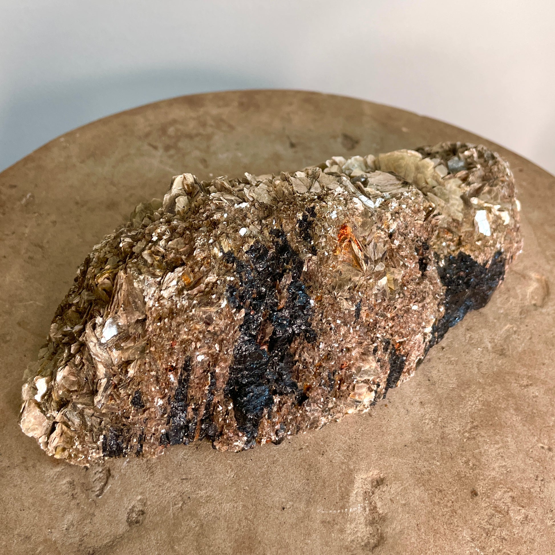 Black Tourmaline and Mica Cluster sitting on a stone with a white background.