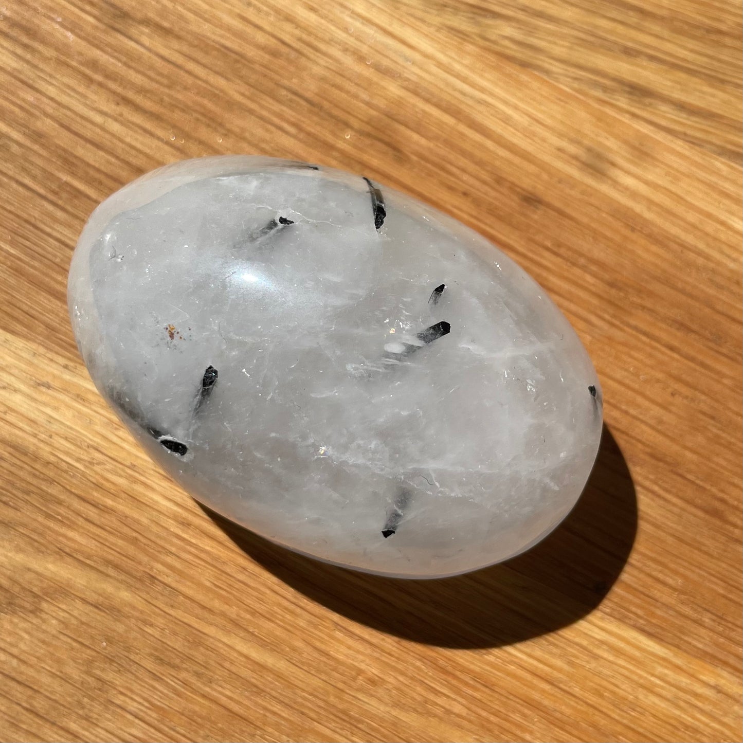 Tourmaline Quartz Palm Stone sitting on a wooden background.