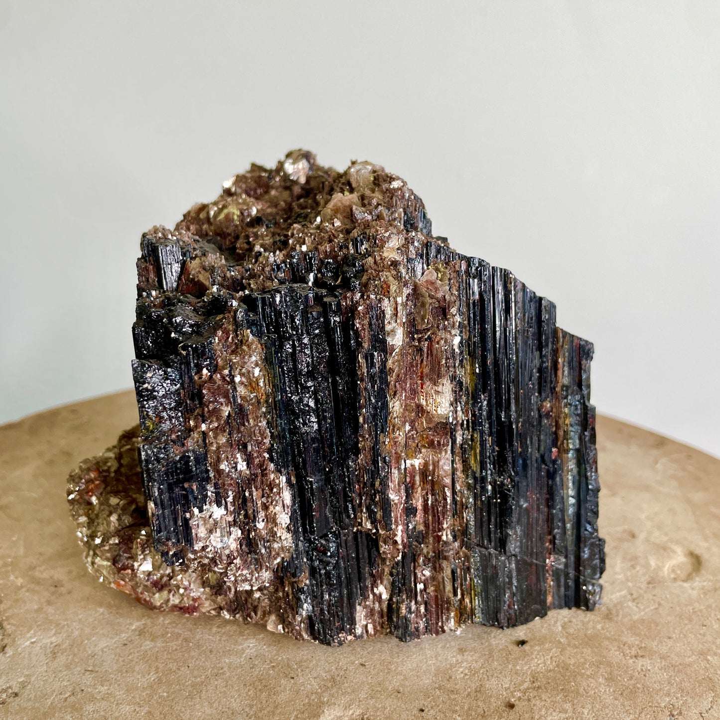 Black Tourmaline and Mica Cluster sitting on a stone with a white background.